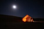 Lit desert camp tent under a moonlit night sky in the Sahara