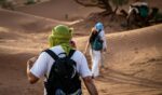 Travellers in turbans walking through the desert dunes with a camel