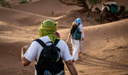 Travellers in turbans walking through the desert dunes with a camel